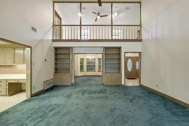 unfurnished living room with a high ceiling, a chandelier, carpet floors, and built in shelves