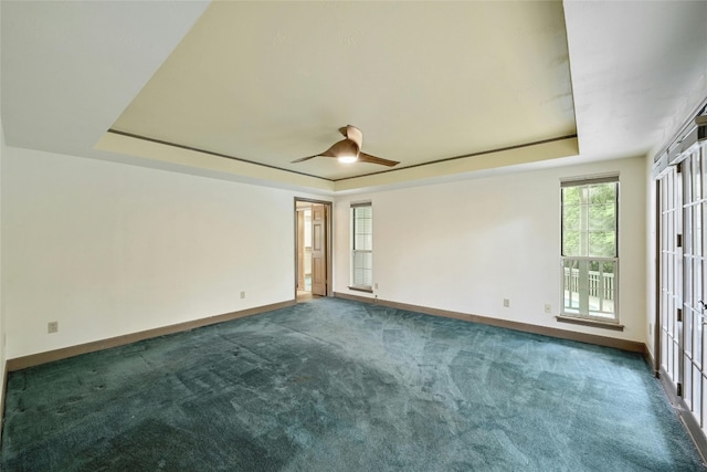 unfurnished room with ceiling fan, a raised ceiling, and dark colored carpet