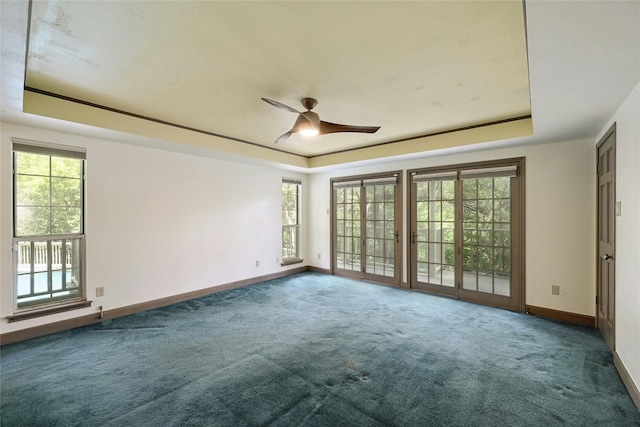 spare room with ceiling fan, a tray ceiling, plenty of natural light, and dark colored carpet