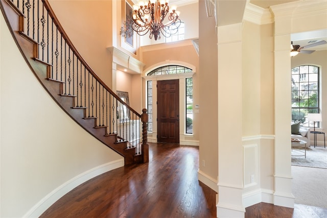 entryway with ceiling fan with notable chandelier, crown molding, dark wood-type flooring, and a high ceiling