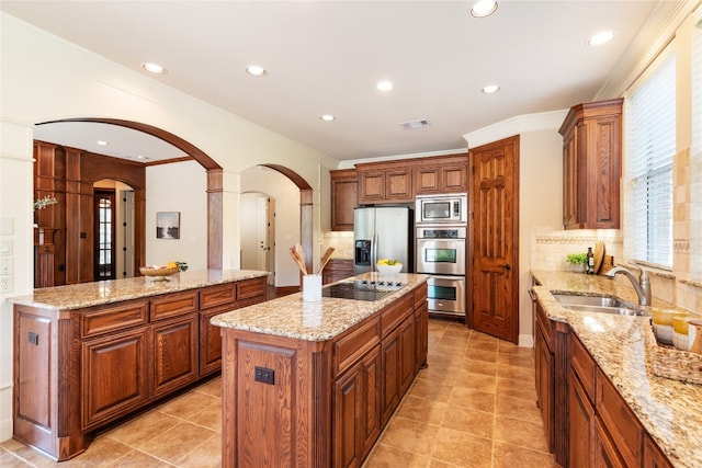 kitchen with stainless steel appliances, light stone counters, a kitchen island, and sink