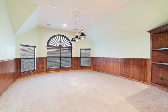 empty room featuring lofted ceiling, wooden walls, a chandelier, and light colored carpet