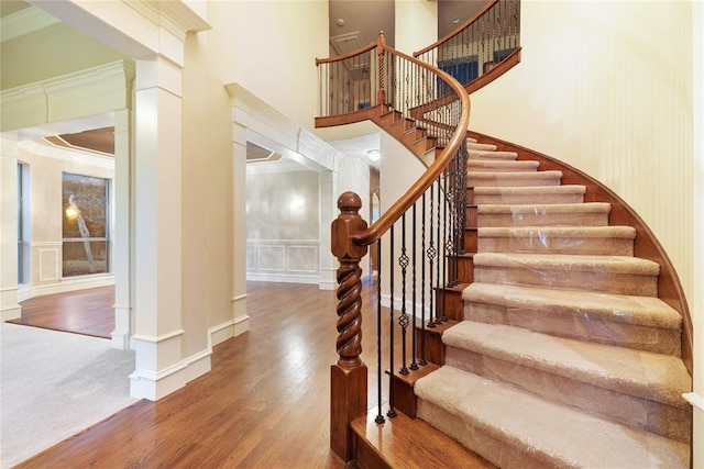 staircase featuring crown molding, hardwood / wood-style floors, and a high ceiling