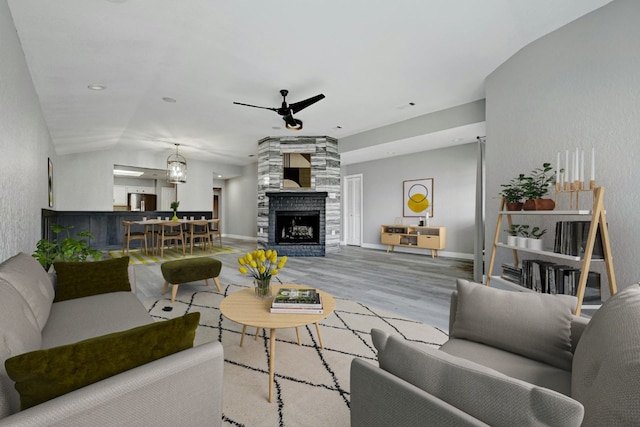 living room featuring light wood-type flooring, vaulted ceiling, a large fireplace, and ceiling fan