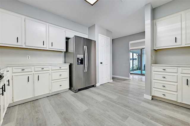 kitchen with light wood-type flooring, stainless steel fridge, and white cabinetry