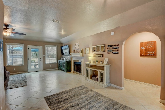 living room with ceiling fan, light tile patterned flooring, lofted ceiling, and a textured ceiling