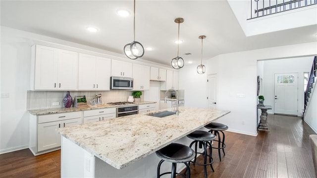 kitchen featuring stainless steel appliances, dark wood-type flooring, white cabinetry, hanging light fixtures, and an island with sink