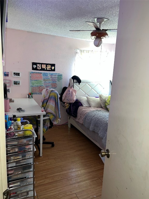 bedroom with ceiling fan, hardwood / wood-style flooring, and a textured ceiling