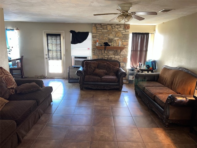 living room with a textured ceiling, cooling unit, a stone fireplace, and ceiling fan