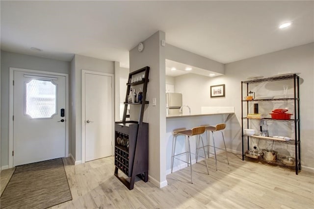 kitchen featuring a breakfast bar, freestanding refrigerator, baseboards, and light wood finished floors