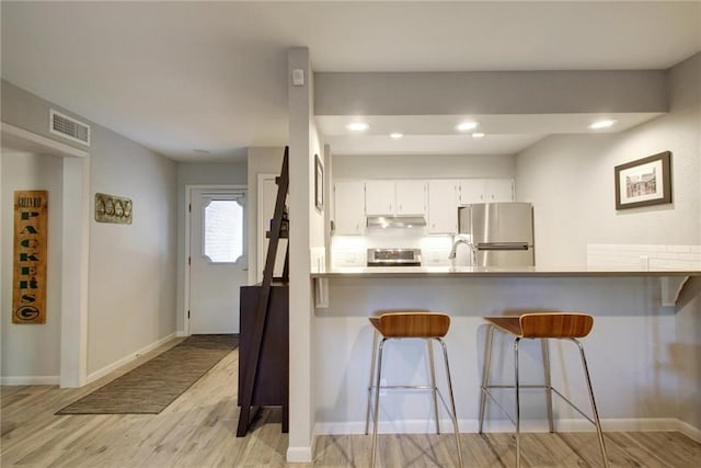 kitchen with a breakfast bar area, a peninsula, stove, visible vents, and freestanding refrigerator