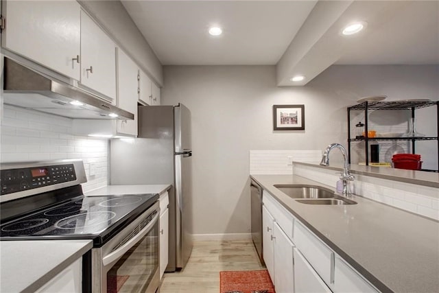 kitchen with light wood finished floors, stainless steel appliances, white cabinetry, a sink, and under cabinet range hood