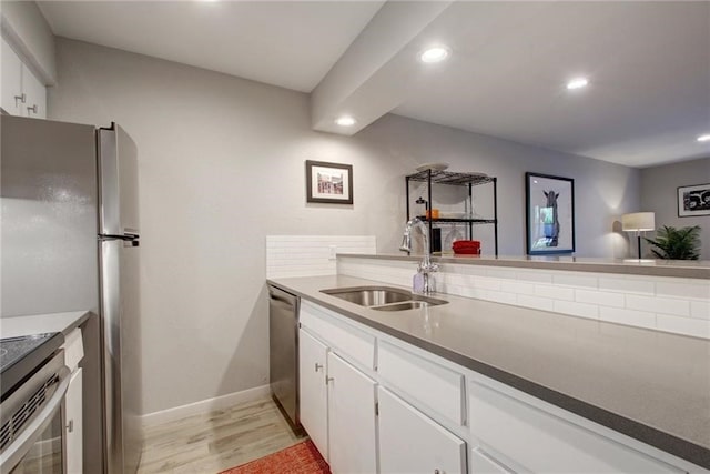 kitchen with light wood finished floors, appliances with stainless steel finishes, white cabinetry, a sink, and recessed lighting