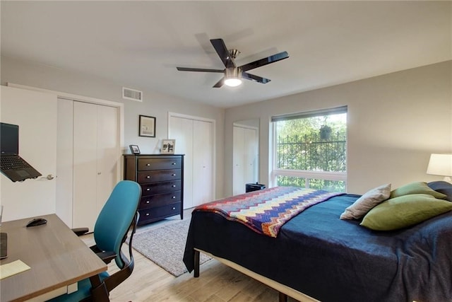 bedroom featuring visible vents, ceiling fan, light wood-style flooring, and two closets