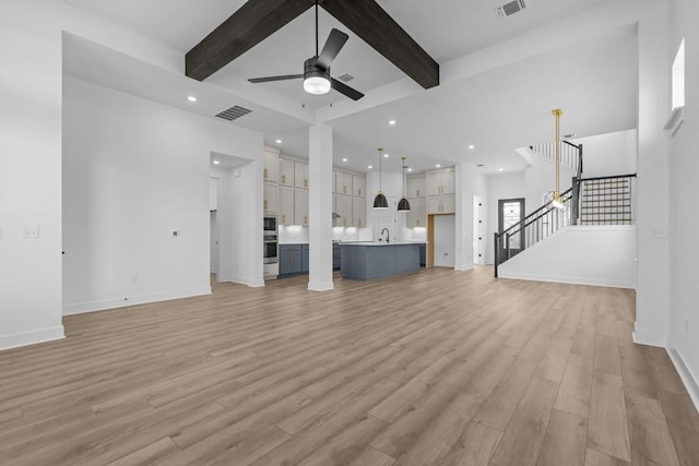 unfurnished living room with stairs, beam ceiling, light wood-style flooring, and visible vents