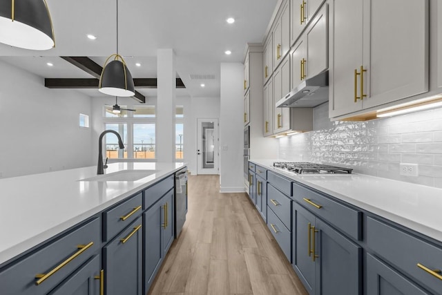 kitchen with under cabinet range hood, appliances with stainless steel finishes, light countertops, and a sink