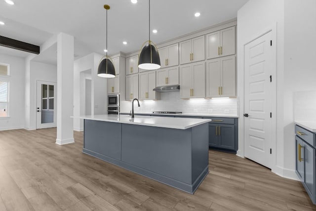 kitchen featuring tasteful backsplash, under cabinet range hood, light countertops, light wood-style floors, and a sink