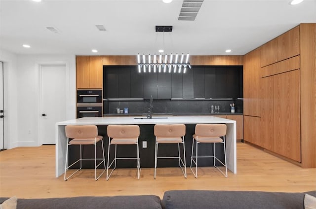 kitchen featuring a kitchen bar, a kitchen island with sink, and light hardwood / wood-style flooring