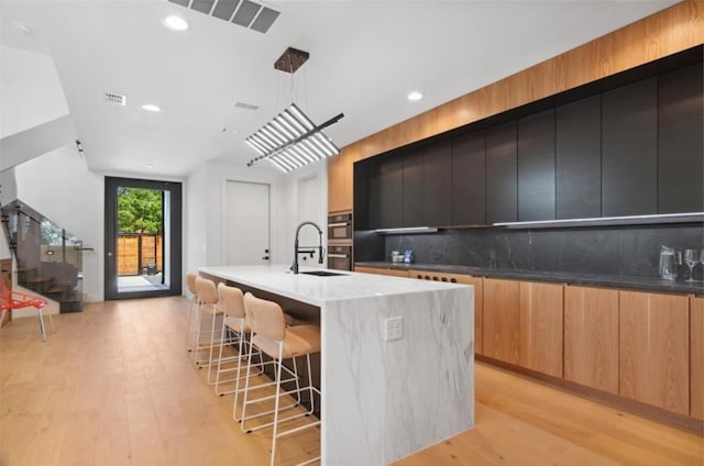 kitchen with hanging light fixtures, sink, a large island, backsplash, and light hardwood / wood-style floors