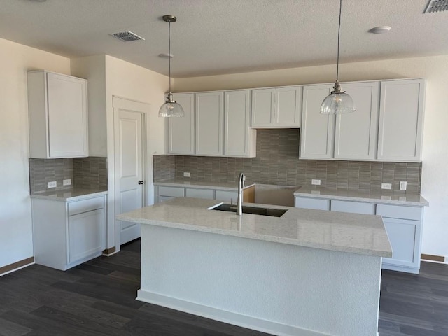 kitchen with a kitchen island with sink, white cabinetry, sink, and hanging light fixtures