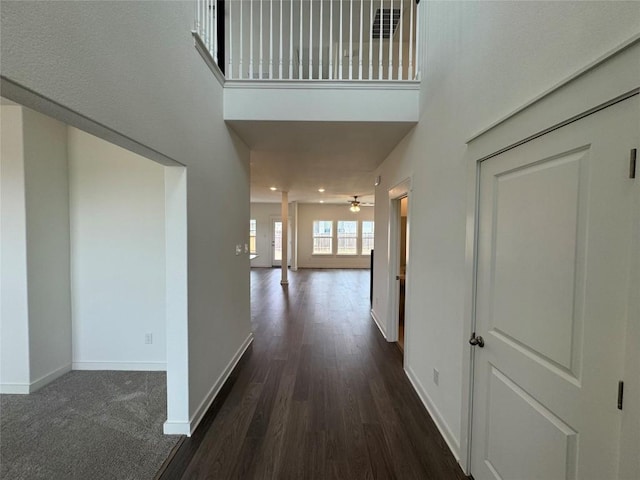 hallway featuring dark wood-style floors, a high ceiling, recessed lighting, and baseboards