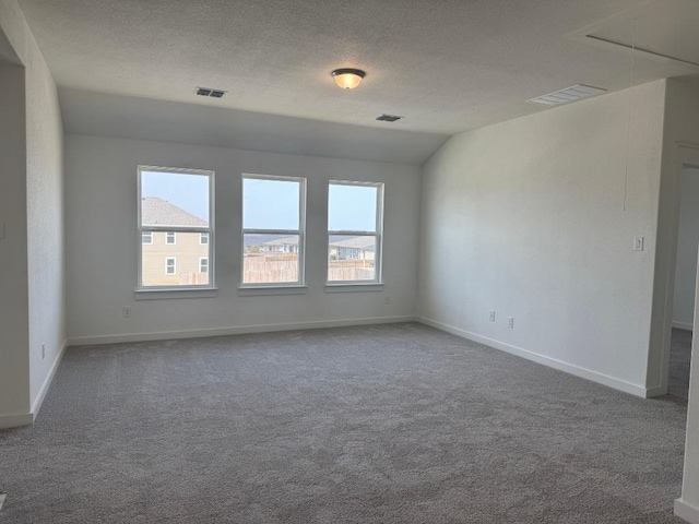 empty room with visible vents, a textured ceiling, carpet flooring, and attic access