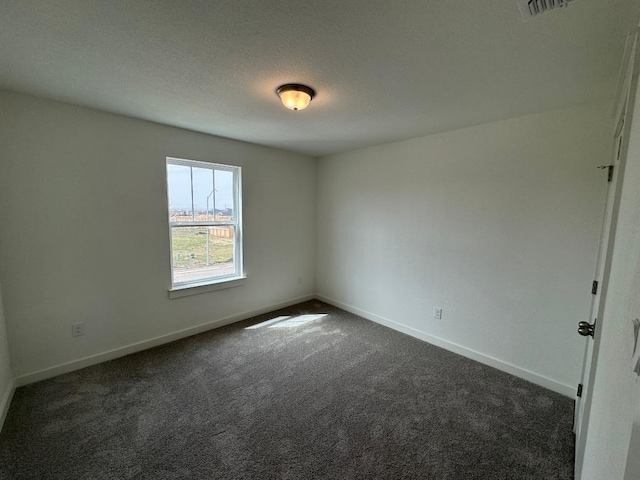 empty room with a textured ceiling, dark carpet, visible vents, and baseboards