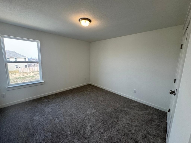 unfurnished room featuring a textured ceiling, dark carpet, and baseboards