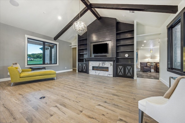 living room with wood-type flooring, beam ceiling, an inviting chandelier, and a high end fireplace