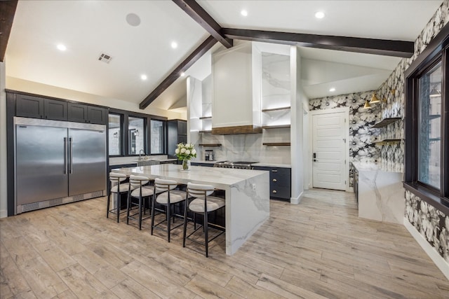 kitchen featuring light stone counters, a kitchen island, light hardwood / wood-style flooring, stainless steel appliances, and lofted ceiling with beams