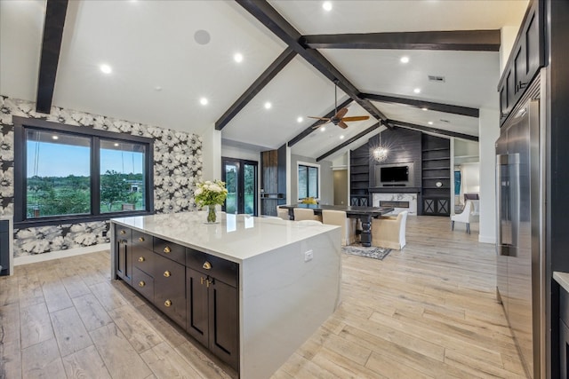 kitchen featuring light hardwood / wood-style floors, lofted ceiling with beams, light stone counters, ceiling fan, and a large island