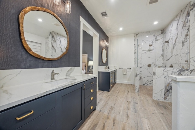 bathroom featuring wood-type flooring, vanity, tile walls, and a tile shower