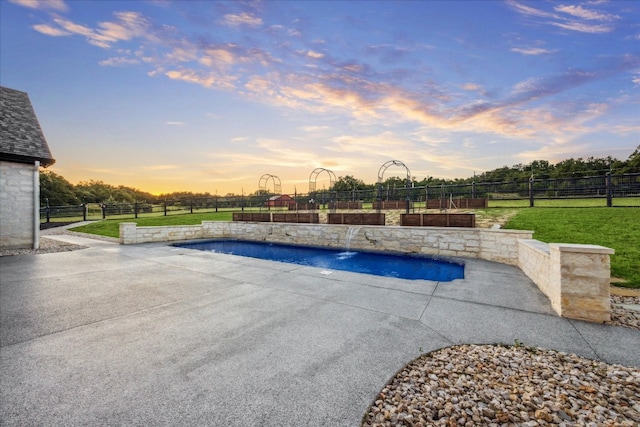 pool at dusk with pool water feature, a patio, and a yard