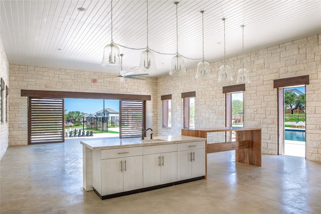 kitchen with a kitchen island with sink, sink, white cabinets, hanging light fixtures, and light stone countertops