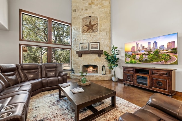 living room featuring a high ceiling, a healthy amount of sunlight, a stone fireplace, and concrete flooring