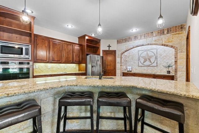 kitchen with appliances with stainless steel finishes, hanging light fixtures, a breakfast bar area, and light stone counters