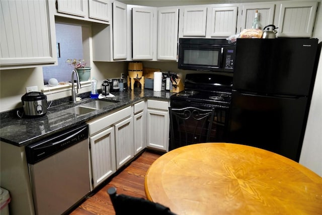 kitchen with sink, dark hardwood / wood-style flooring, dark stone countertops, white cabinets, and black appliances