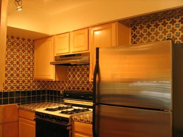 505 W 7th St Unit 108, Austin, TX 78701 - kitchen with under cabinet range hood, freestanding refrigerator, white gas range oven, decorative backsplash, and wallpapered walls