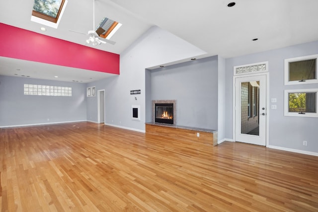 unfurnished living room featuring a skylight, high vaulted ceiling, ceiling fan, and light hardwood / wood-style flooring