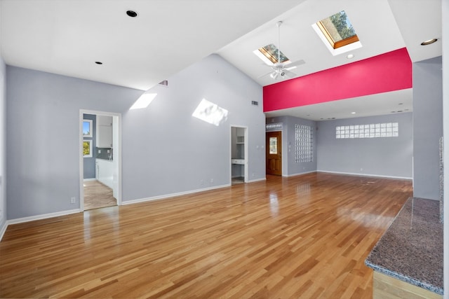 unfurnished living room with hardwood / wood-style flooring, a skylight, high vaulted ceiling, and ceiling fan