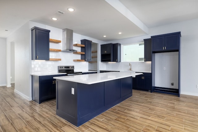 kitchen with light wood-type flooring, backsplash, wall chimney exhaust hood, a kitchen island, and stainless steel range with electric cooktop