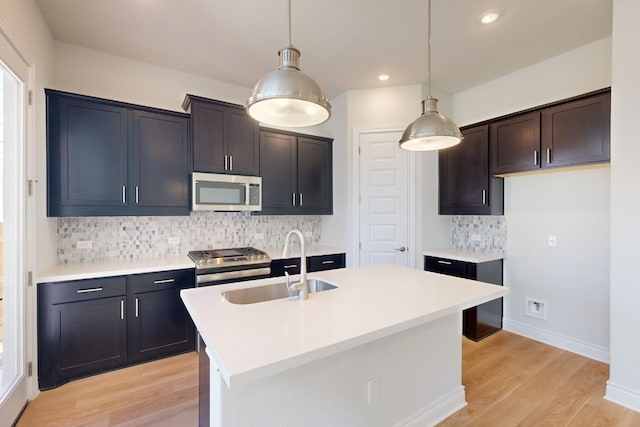 kitchen featuring pendant lighting, a center island with sink, sink, light wood-type flooring, and stainless steel appliances