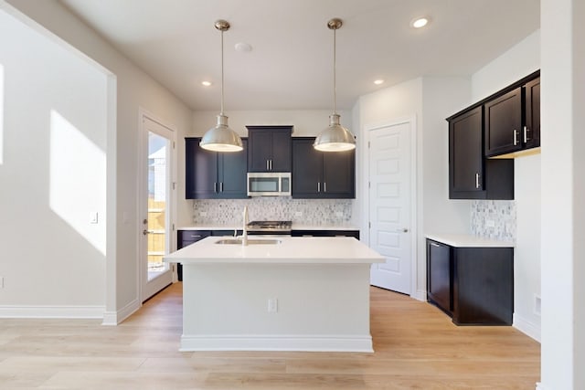 kitchen with sink, light hardwood / wood-style flooring, hanging light fixtures, and a kitchen island with sink