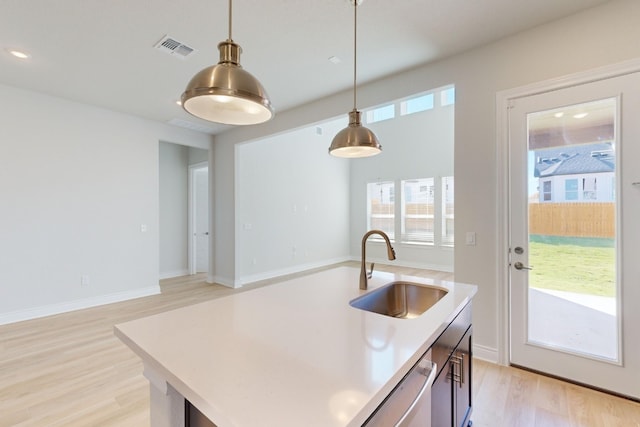 kitchen featuring pendant lighting, a center island with sink, sink, light hardwood / wood-style flooring, and stainless steel dishwasher