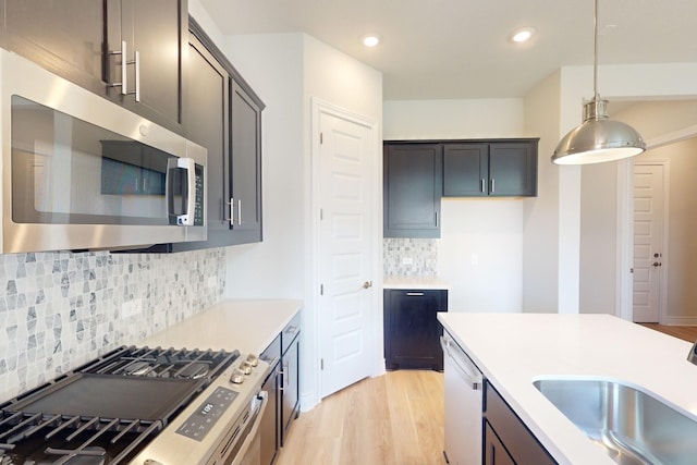 kitchen with light wood-type flooring, tasteful backsplash, stainless steel appliances, sink, and pendant lighting