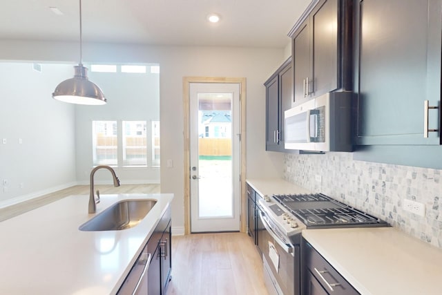 kitchen featuring sink, stainless steel appliances, tasteful backsplash, pendant lighting, and light hardwood / wood-style floors