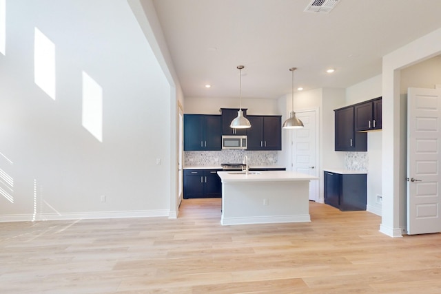 kitchen featuring hanging light fixtures, decorative backsplash, a center island with sink, and light hardwood / wood-style floors