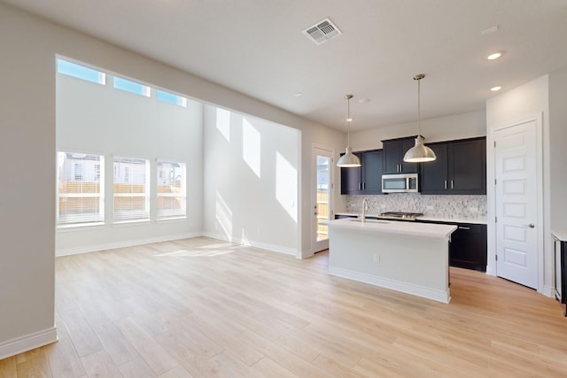 kitchen featuring pendant lighting, an island with sink, light hardwood / wood-style floors, and sink