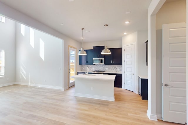 kitchen featuring tasteful backsplash, a kitchen island with sink, sink, light hardwood / wood-style flooring, and hanging light fixtures