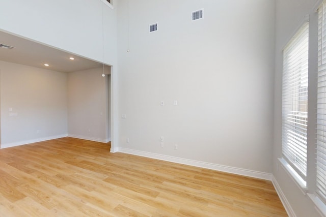 empty room with a wealth of natural light, a towering ceiling, and light hardwood / wood-style floors